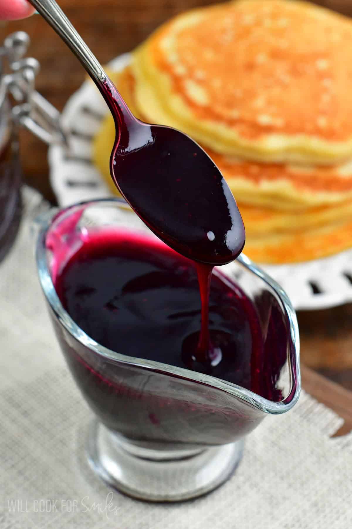 blueberry syrup pouring off spoon into the saucer cup.