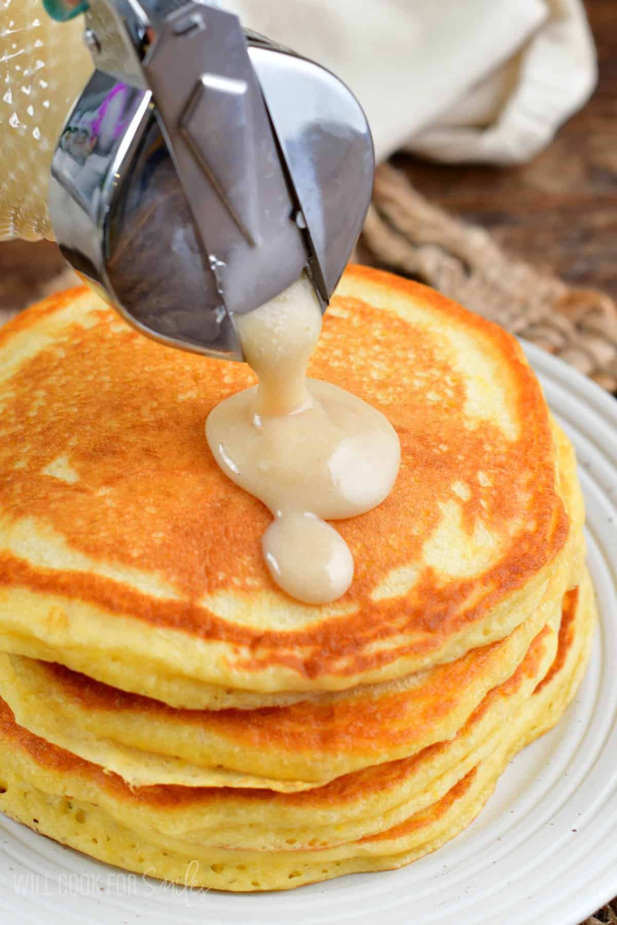 pouring coconut syrup over pancakes on a plate.