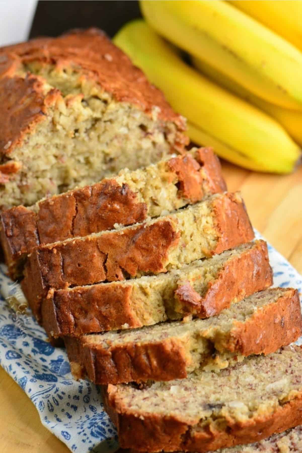 Coconut banana bread sliced up on a wood surface with bananas in the background.