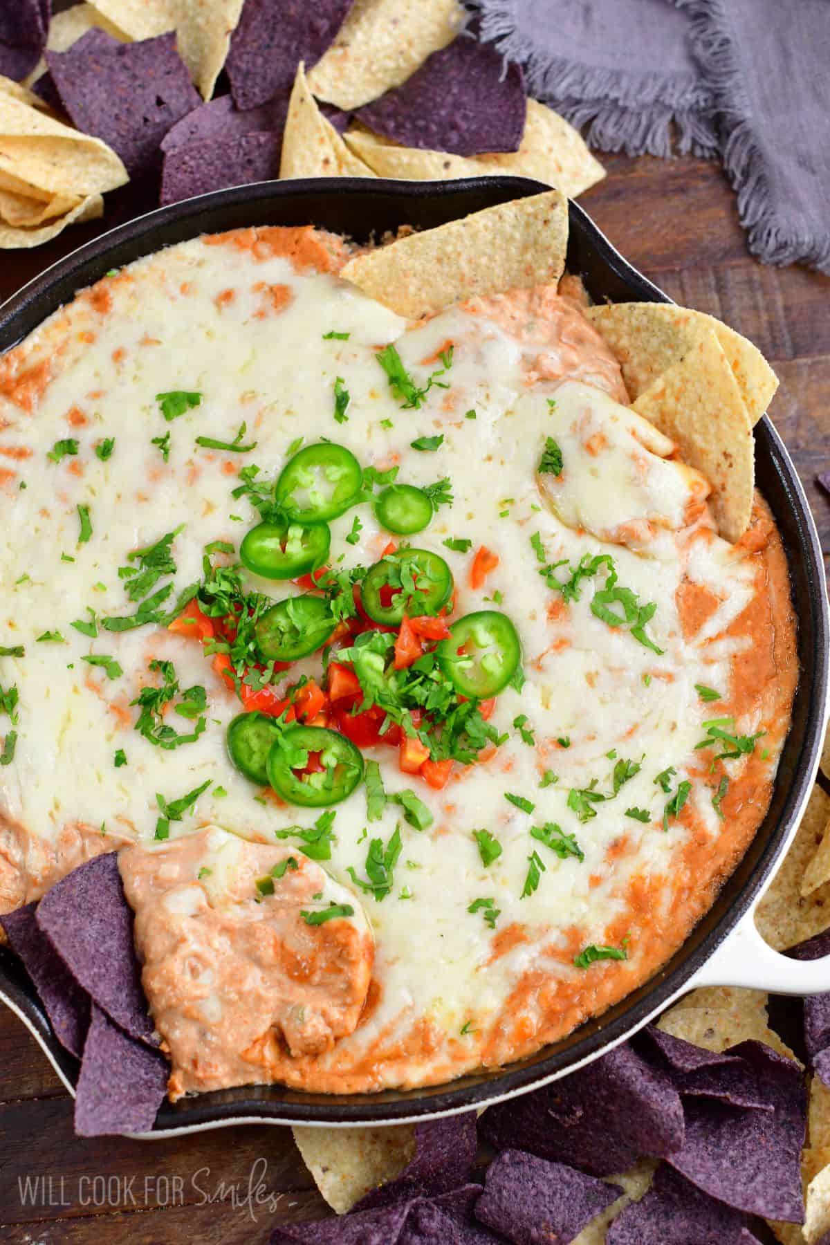 hot bean dip topped with tomatoes, jalapenos, and cilantro in a cast iron skillet with some tortilla chips in it.