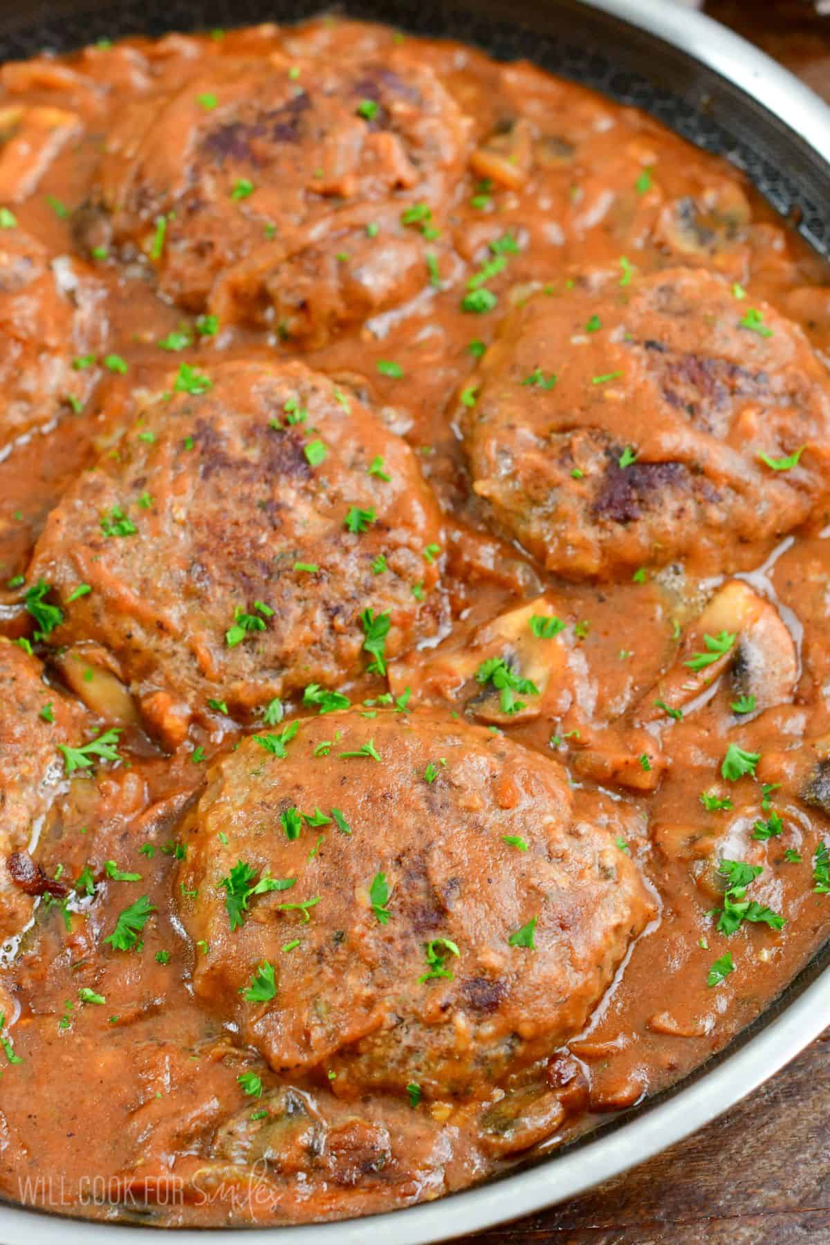 Salisbury Steak in a pan top with parsley on top on a wood surface.