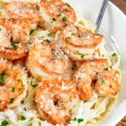 Shrimp alfredo in a white bowl on a burlap tablecloth underneath the bowl.
