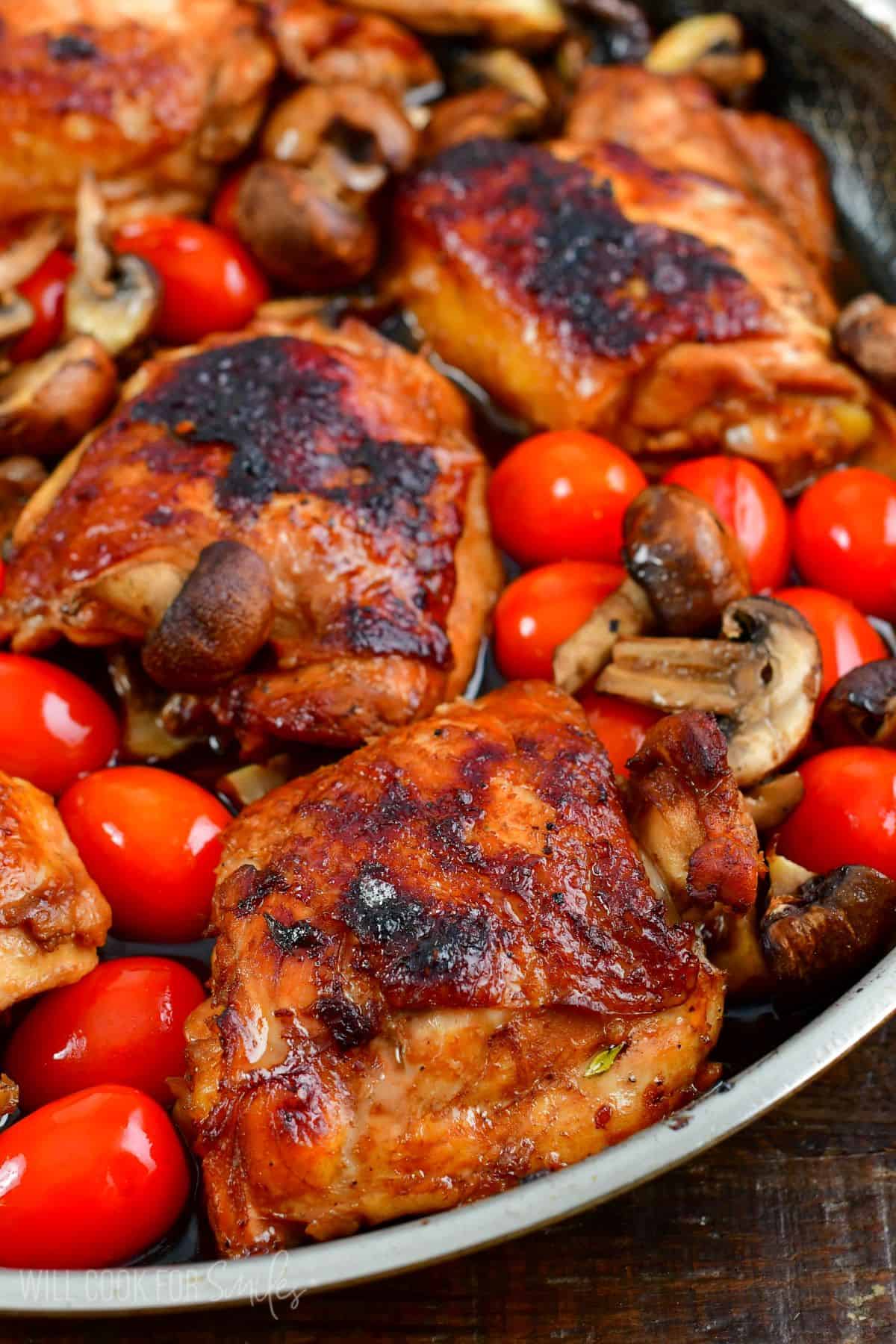 Balsamic baked chicken thighs in a pan with cherry tomatoes and sliced mushrooms.