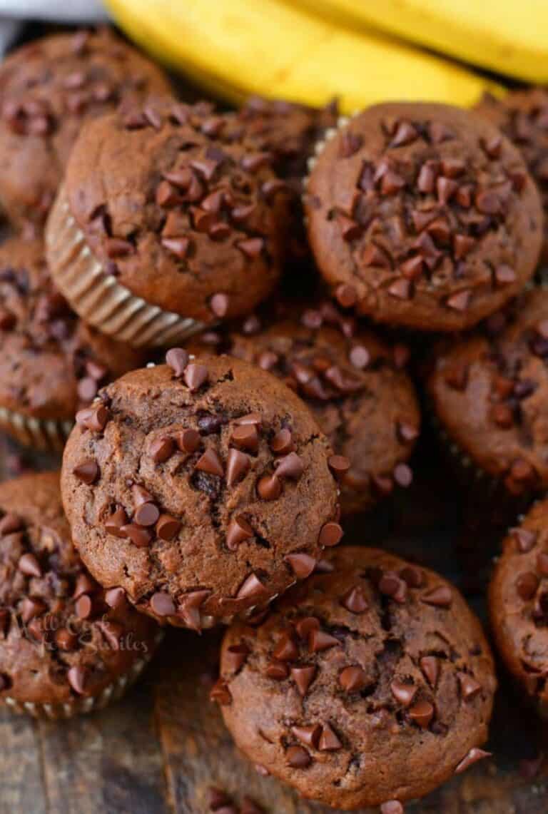 several chocolate banana muffins stacked together next to bananas.