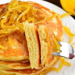 Lemon pancakes lemon peels on top with a cut slice on a fork.