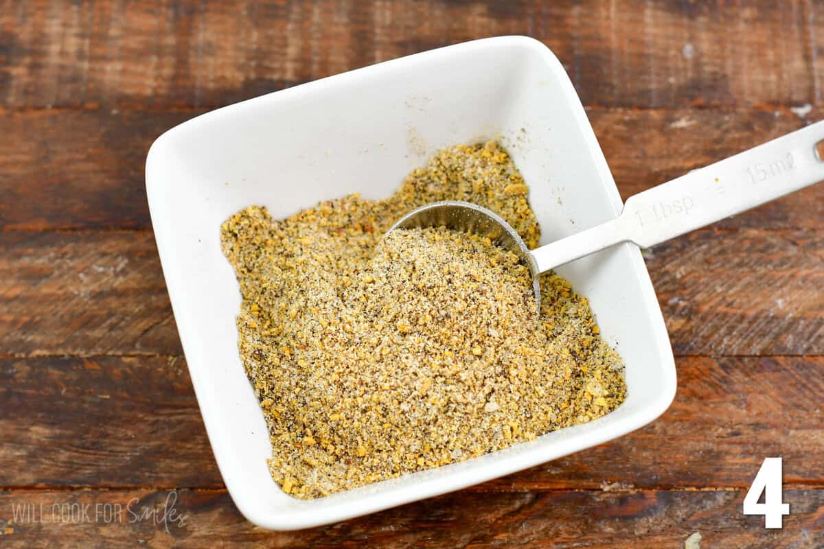 Lemon pepper seasoning mix in a small bowl with a teaspoon in the bowl.