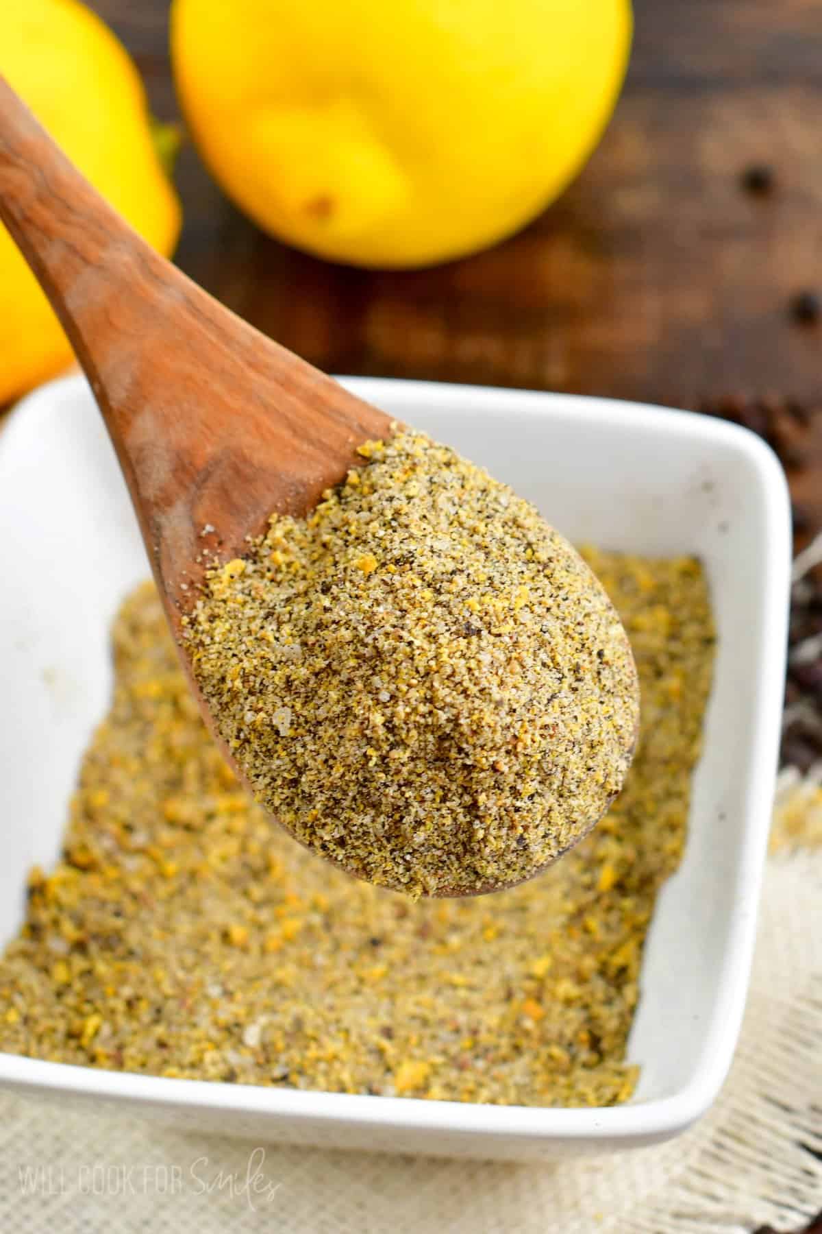 Lemon pepper seasoning in a bowl with a wooden spoon with seasoning on it.