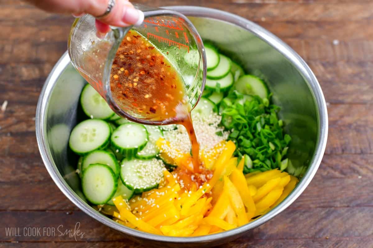 pouring salad dressing into the bowl of cucumber salad.