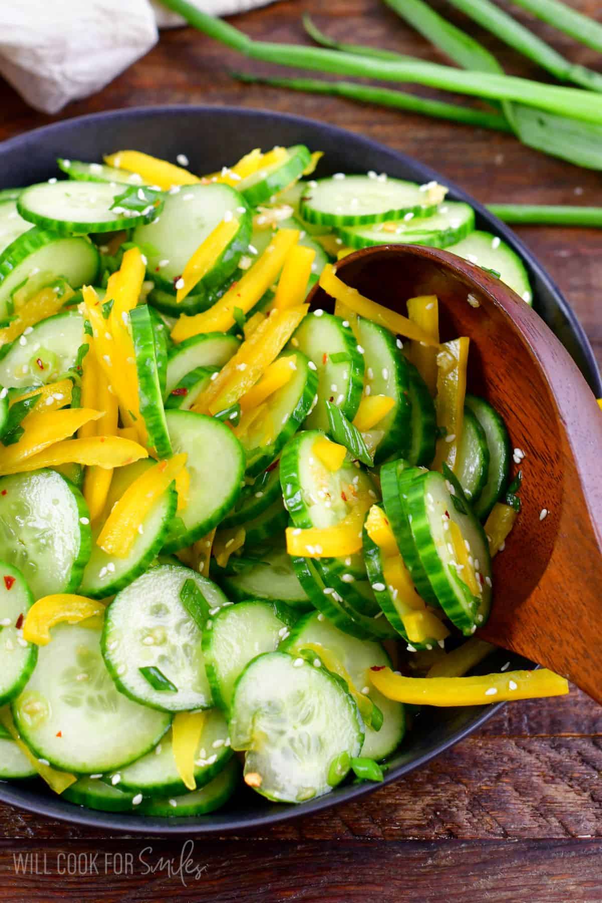 Asian cucumber salad in a bowl with a wooden spoon.