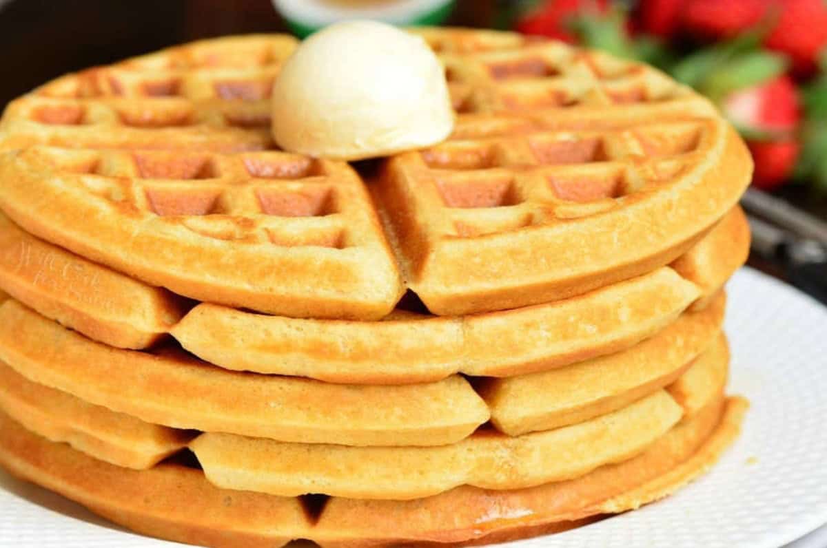 A stack of waffles on a plate with a butter on top.