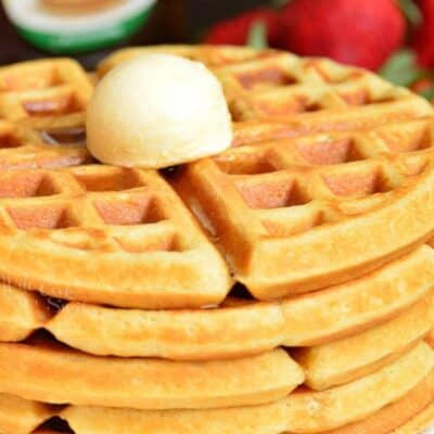 Waffles stacked up on a plate with a dollop of butter on top.