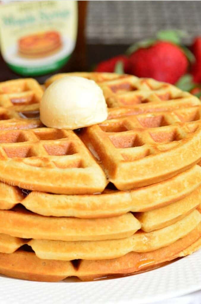 Waffles stacked up on a plate with a dollop of butter on top.