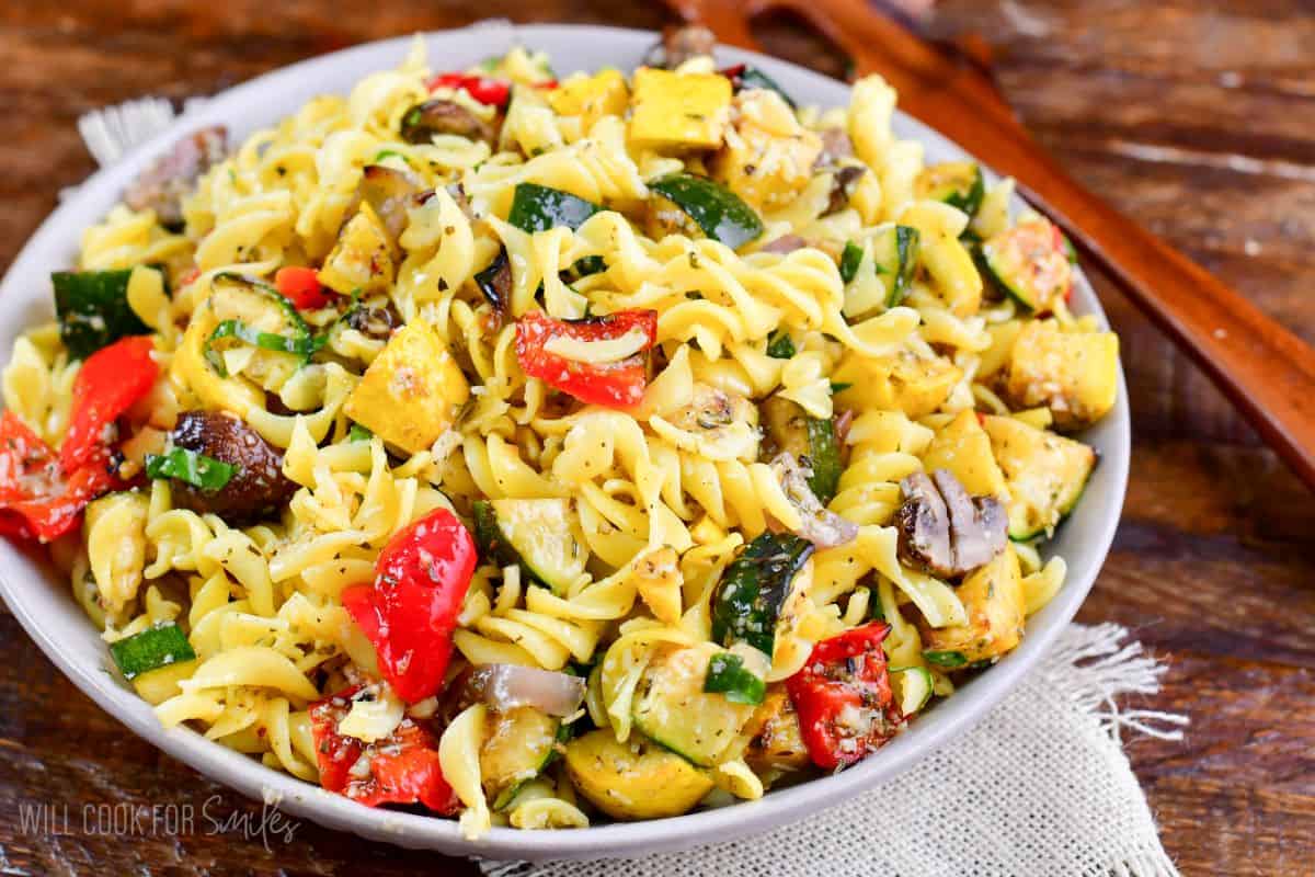 Grilled vegetable pasta salad in a bowl with a wood spoon to the right of the bowl.