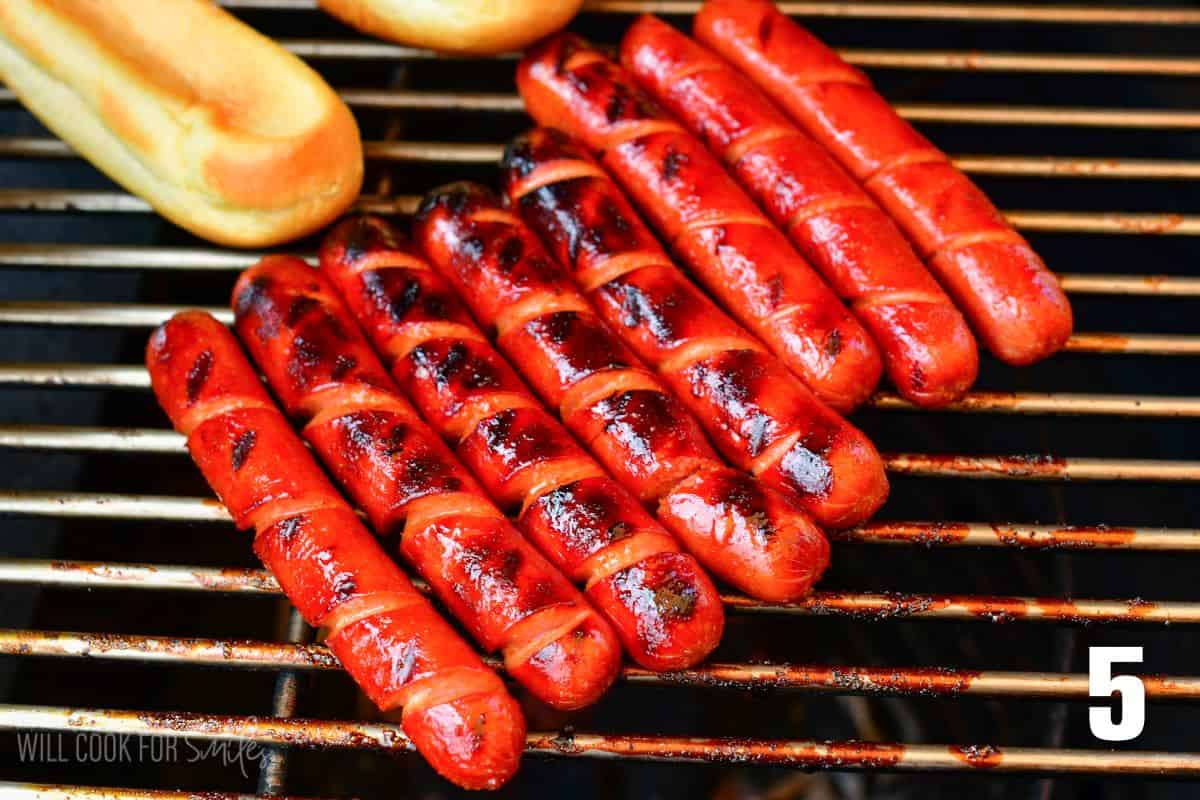 Grilling spiral cut hotdogs next to hot dog buns.