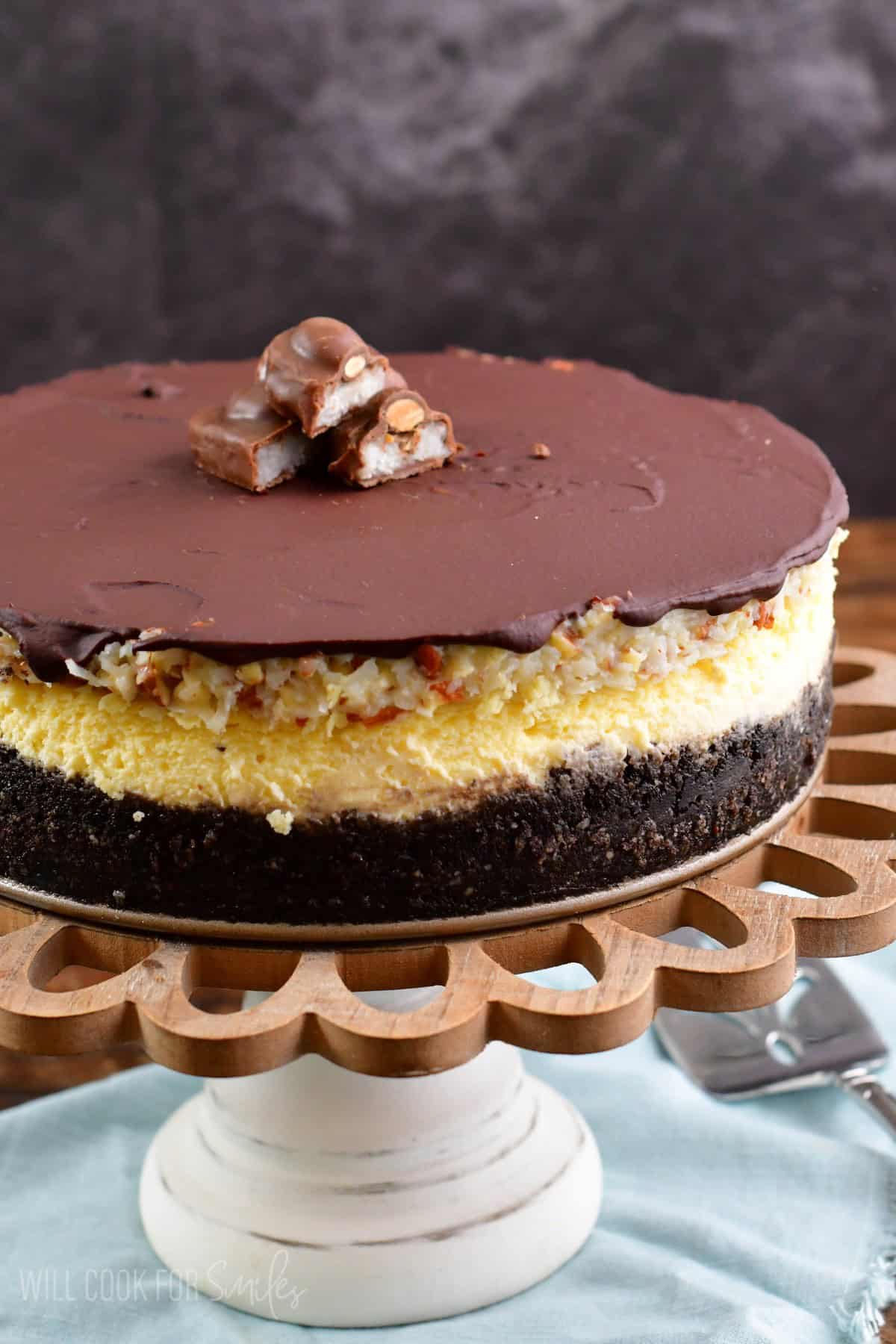 Almond Joy Cheesecake on a cakes stand on a blue cloth napkin.