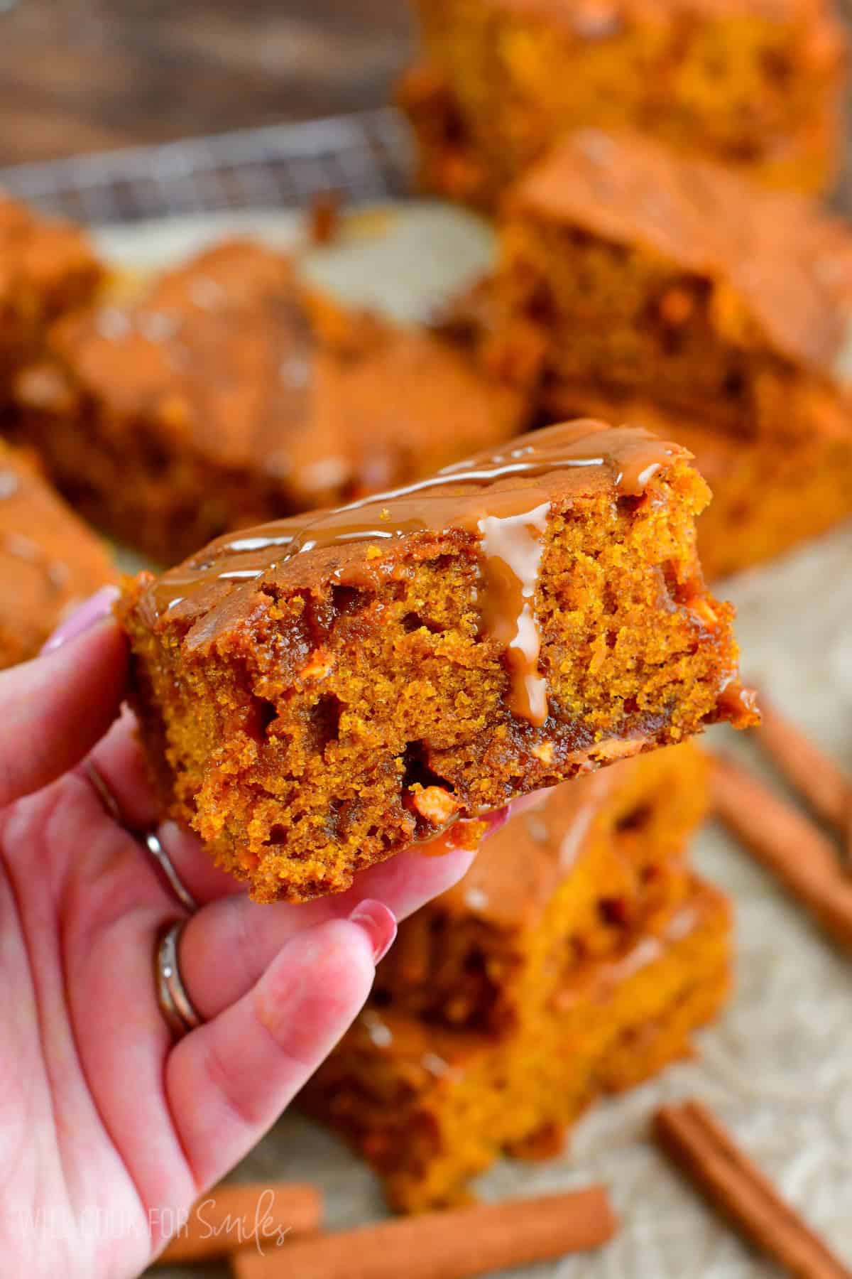 Holding a pumpkin blondie square with the rest of the blondies on parchment paper.