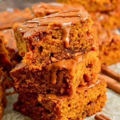 Caramel Pumpkin Blondies stacked on parchment paper with cinnamon sticks around them.