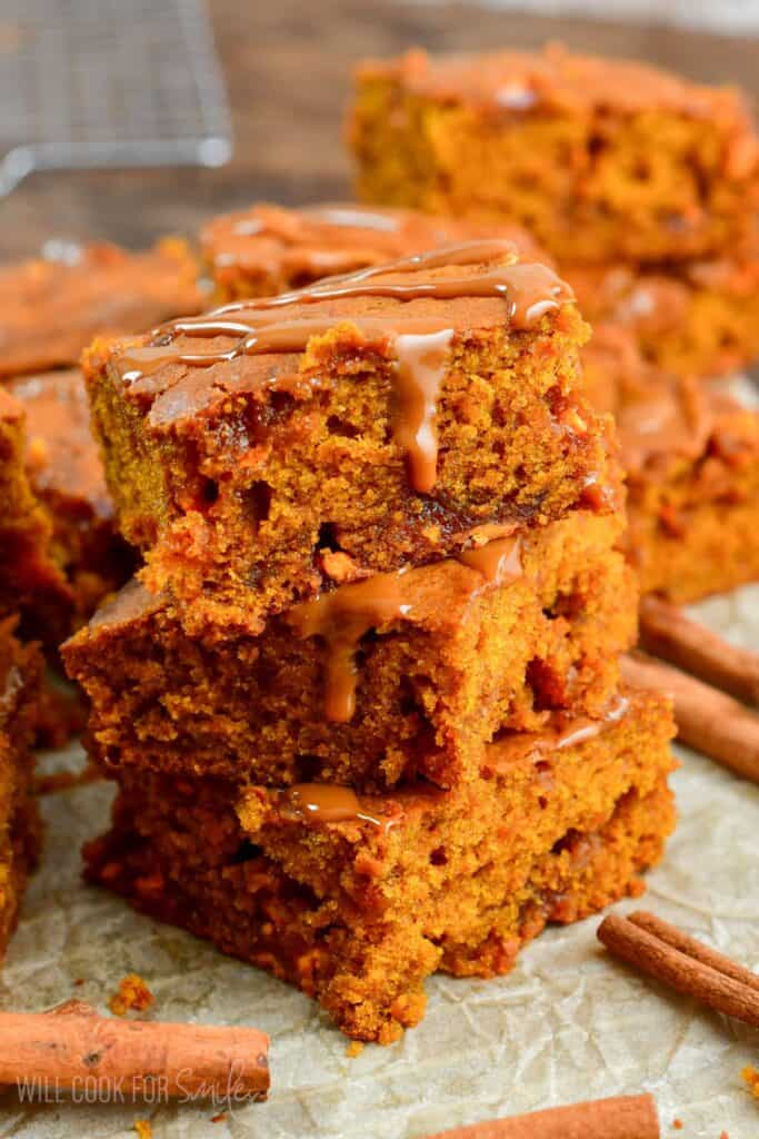 Caramel Pumpkin Blondies stacked on parchment paper with cinnamon sticks around them.