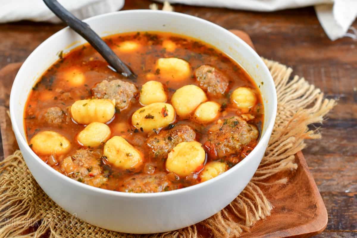 meatballs and gnocchi soup in a bowl on a wooden plate.