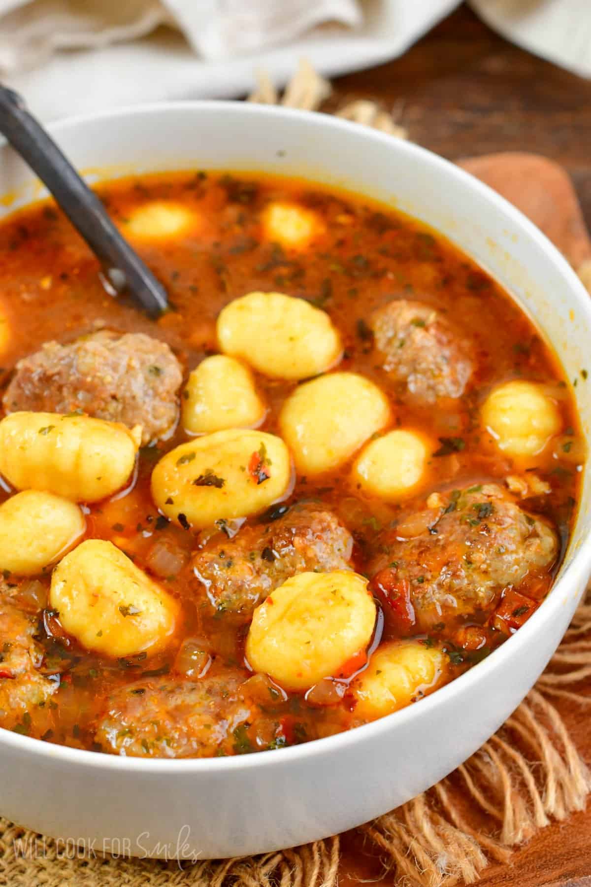 meatball and gnocchi soup in a bowl with a spoon in it.