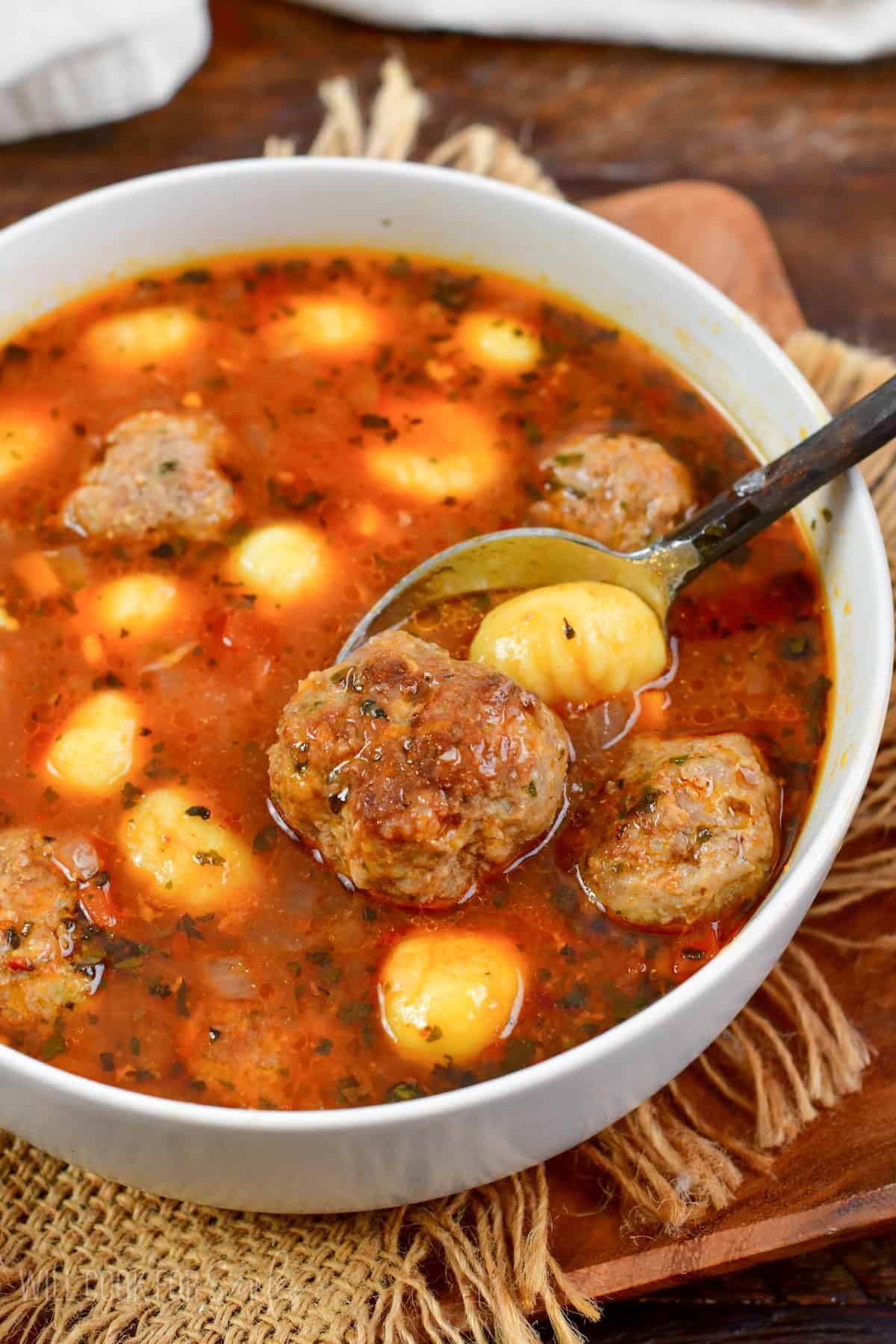 spooning out a meatballs and some gnocchi from the bowl of soup.