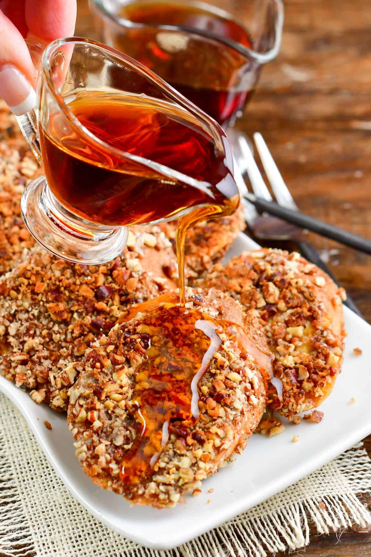 Pecan crusted French toast on a plate pouring syrup over them.