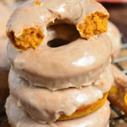 Pumpkin donuts with one torn in half on a wire rack.