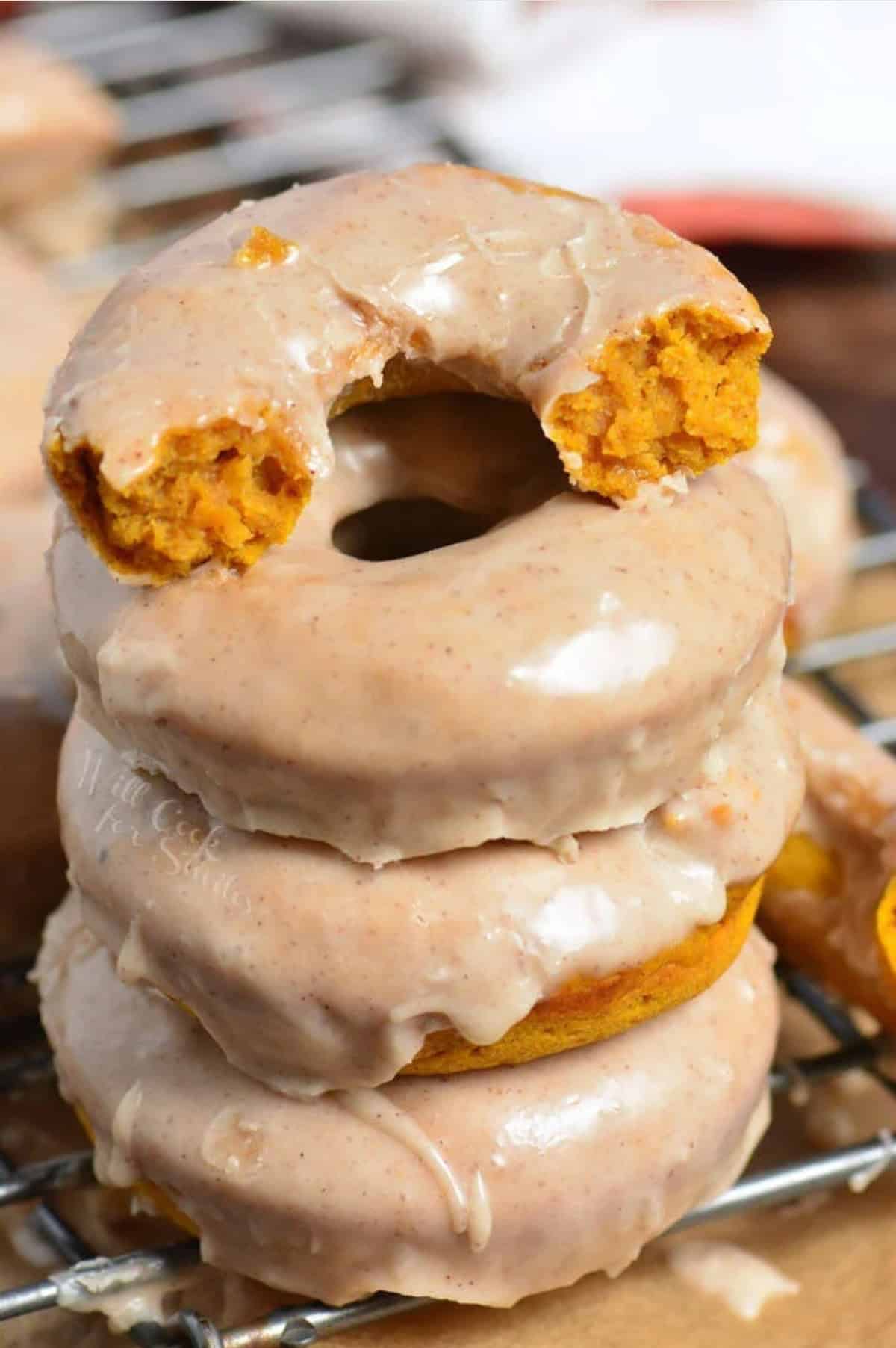 Pumpkin donuts with one torn in half on a wire rack.