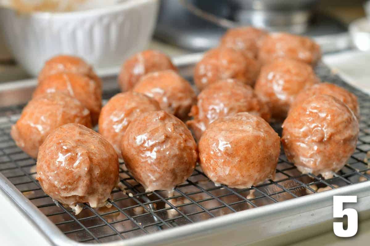 glazed pumpkin donut holes laid out on a wire rack fitted in a baking sheet.