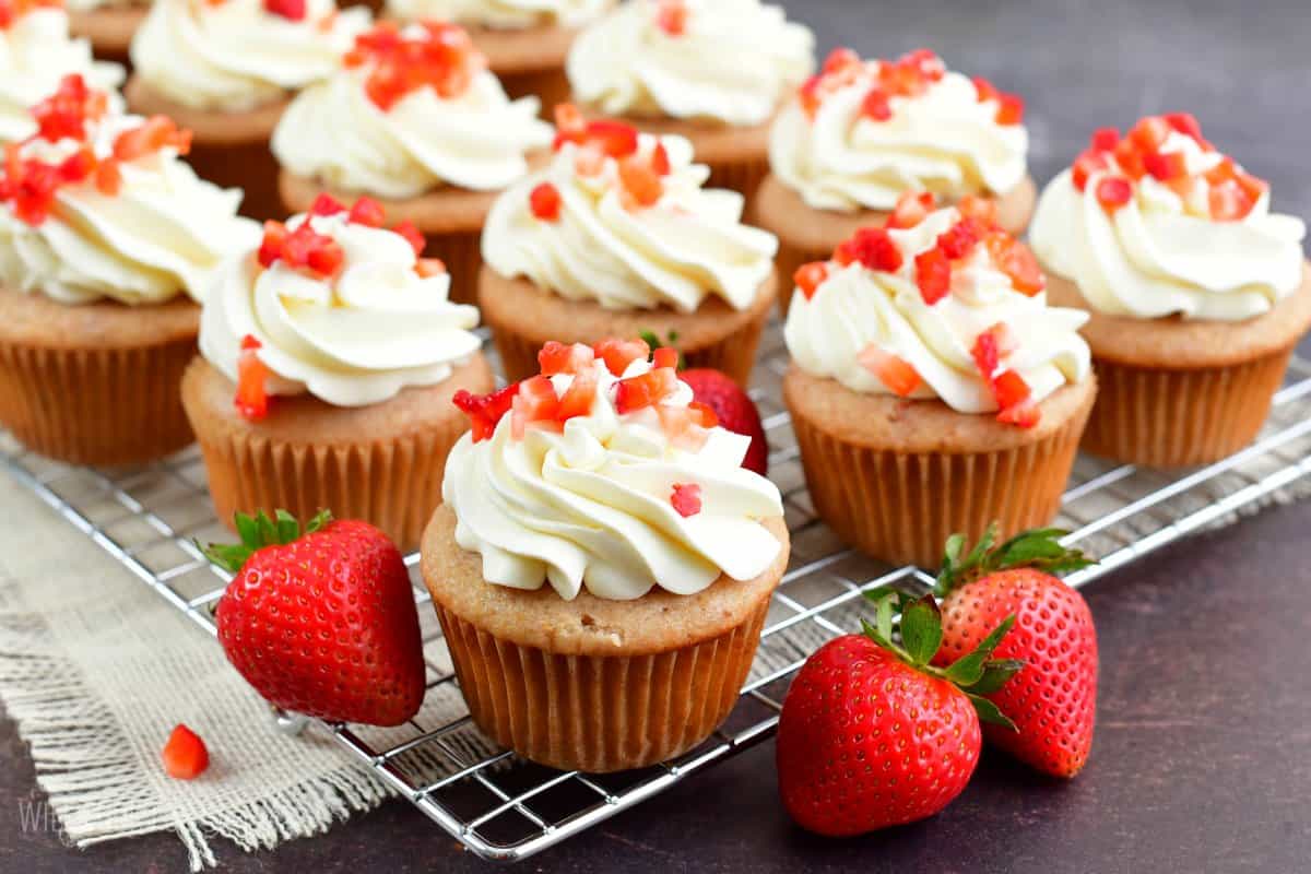 Strawberry cupcakes with frosting and diced strawberries on top on a wire rack.