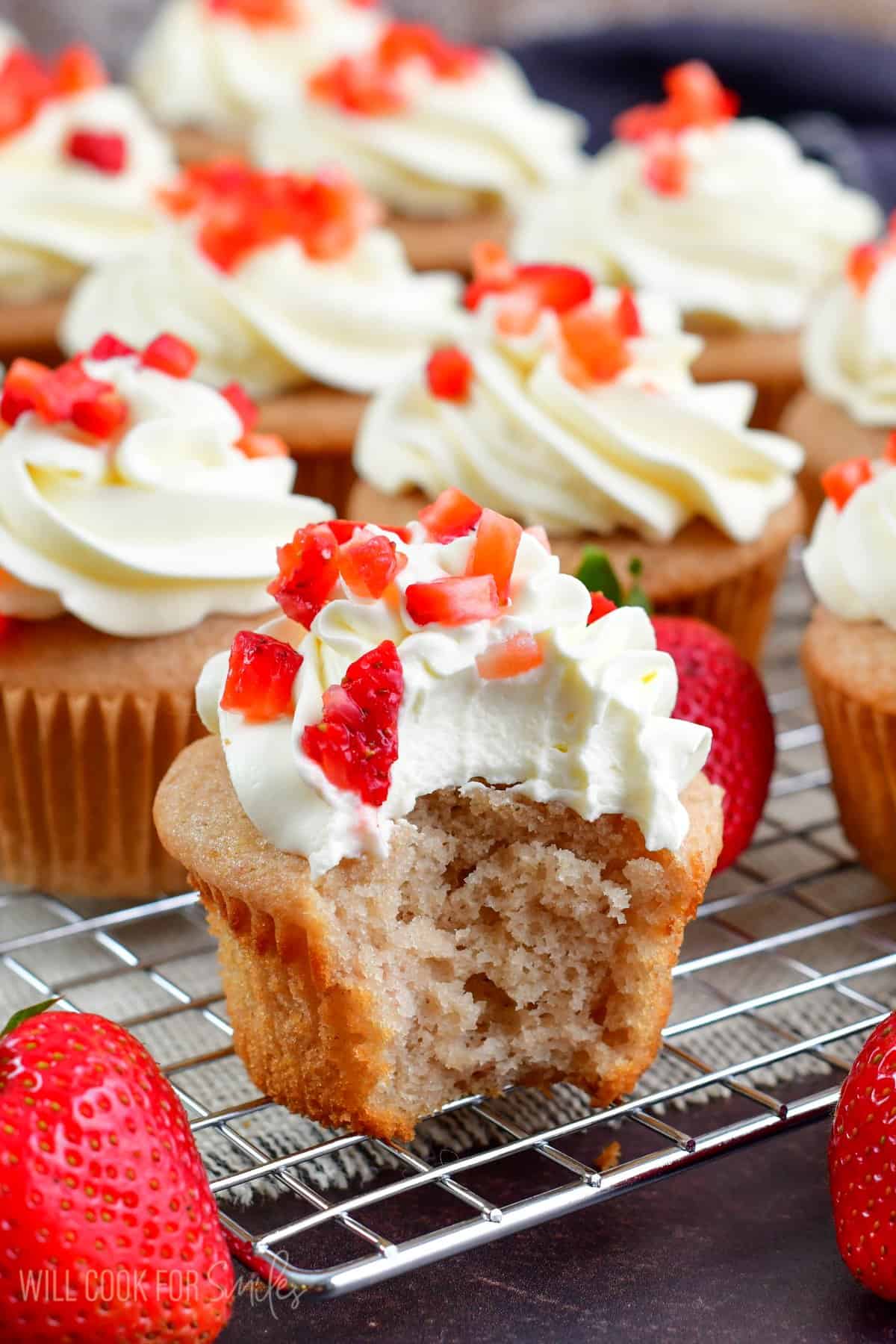 Strawberry Cupcake with a bite taken out of it and the rest of the cupcakes on a wire rack.