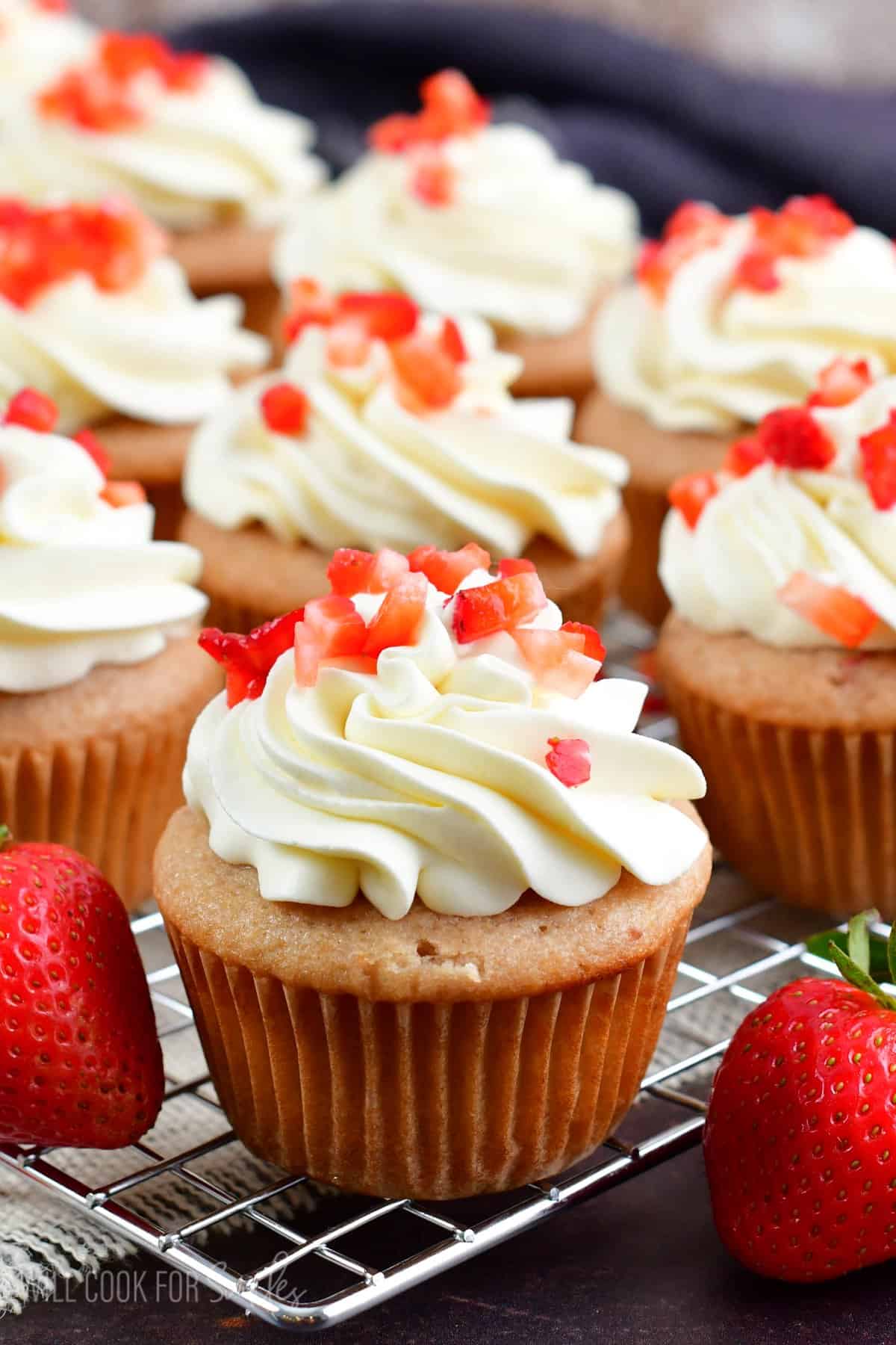 Cupcake with frosting on top and diced up strawberries on a wire rack.