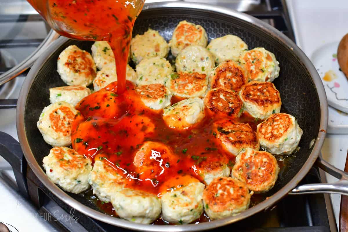 Pouring Thai sweet chili sauce mixture over meatballs that are in a pan.