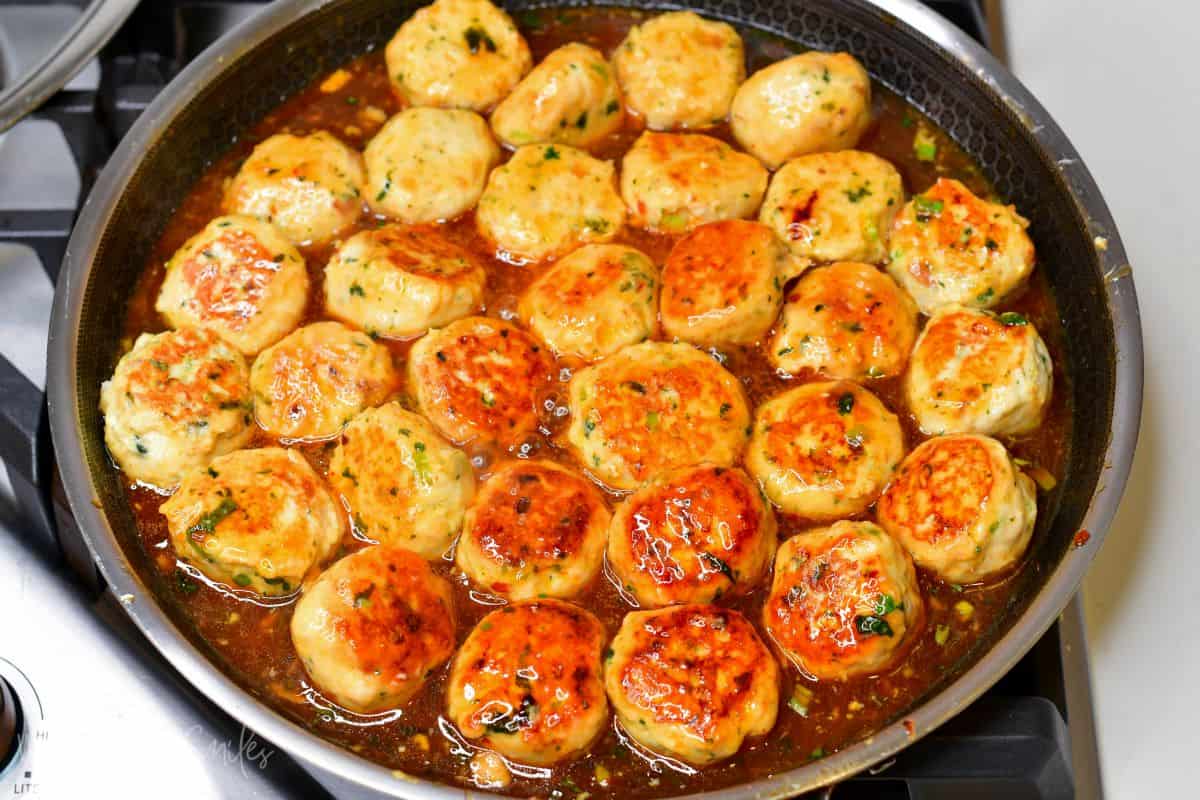 Thai turkey meatballs cooking in the sauce in a pan.