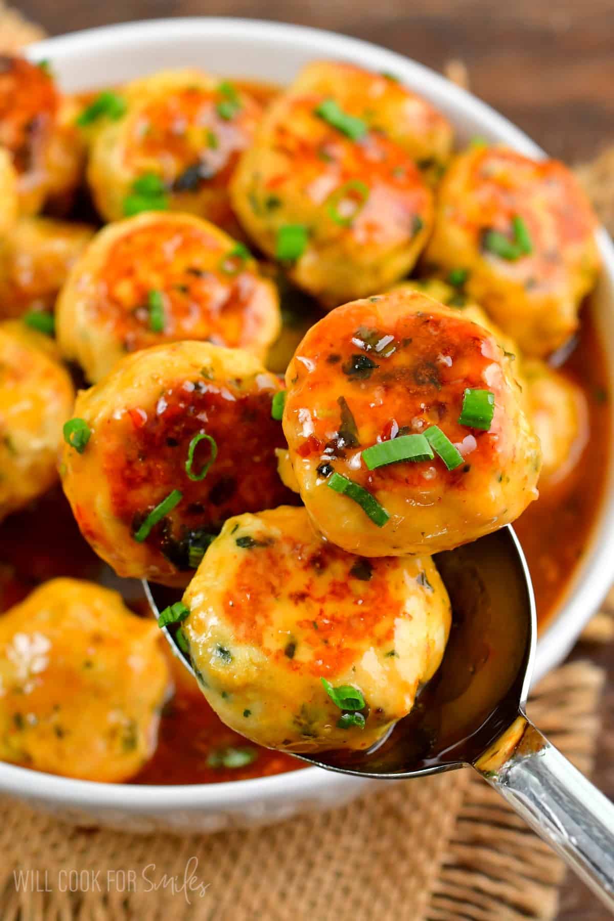 three meatballs on a spoon with the rest of the meatballs in a bowl.