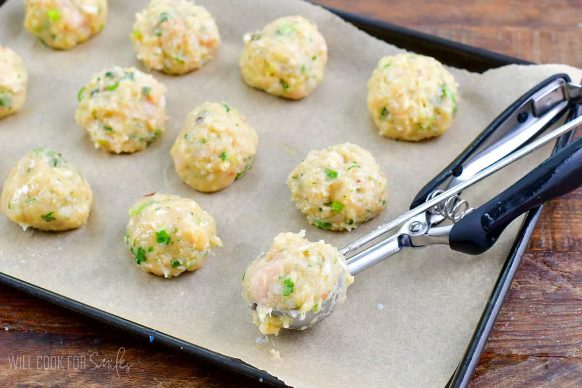 Thai Sweet Chili Turkey Meatballs with a scoop of meatballs on a cookie scoop on a parchment lined baking sheet.