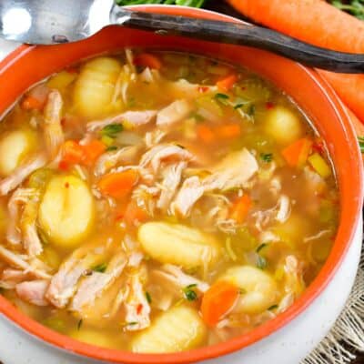 chicken gnocchi soup in a bowl with a spoon on the edge and veggies around.