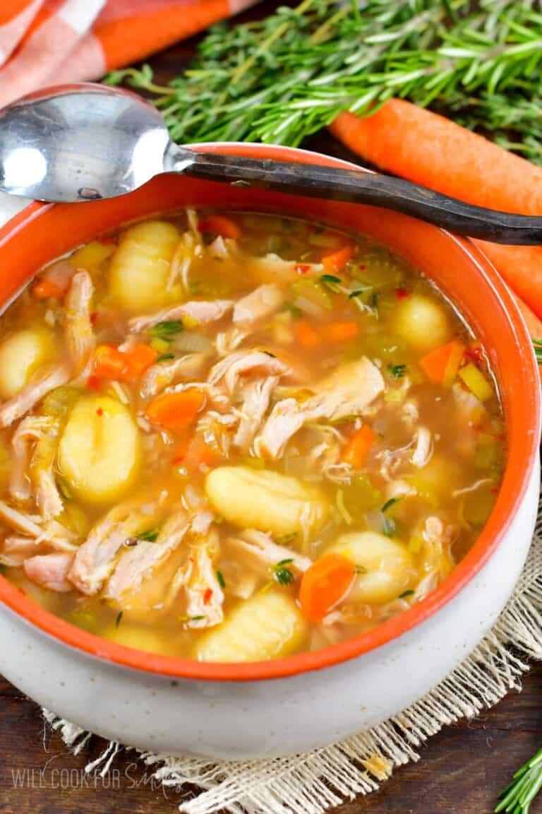 chicken gnocchi soup in a bowl with a spoon on the edge and veggies around.