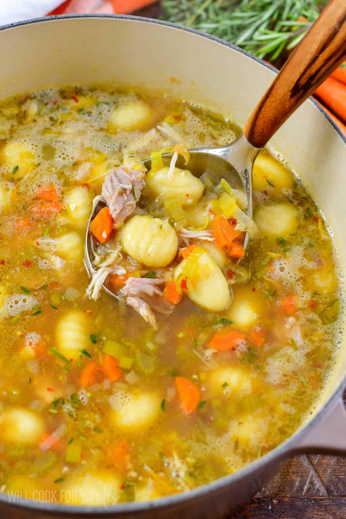 scooping out some chicken gnocchi soup with a ladle from the pot.