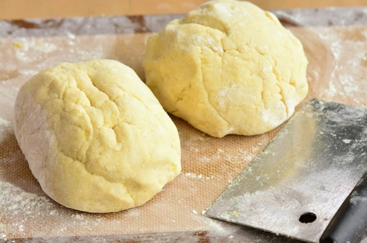 gnocchi dough divided into two equal parts on the floured mat with pastry cutter.