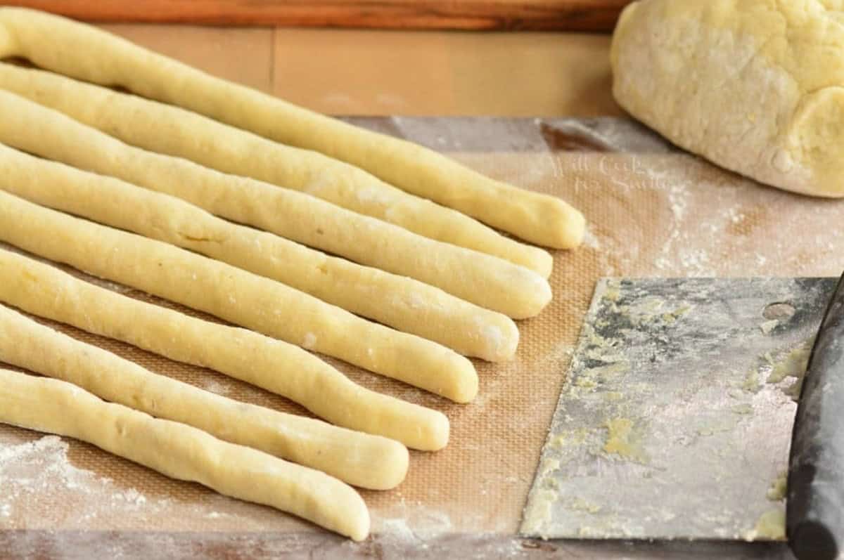 rolled strips of gnocchi dough in the floured mat next to more dough and pastry cutter.