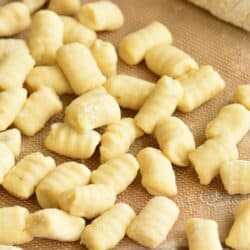 rolled pieces of gnocchi on a silicone mat next to another half of dough.