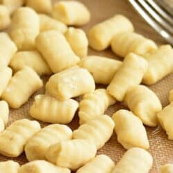 uncooked gnocchi spread on a silicone mat with a fork next to it.