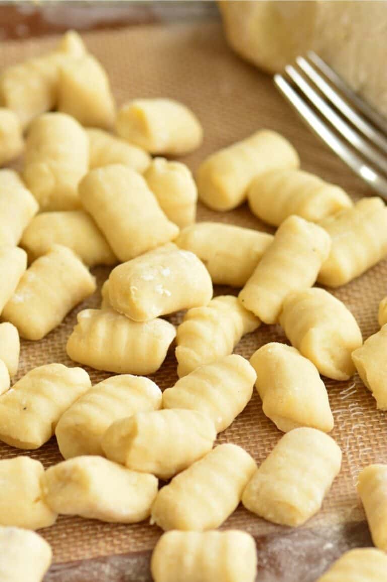 uncooked gnocchi spread on a silicone mat with a fork next to it.