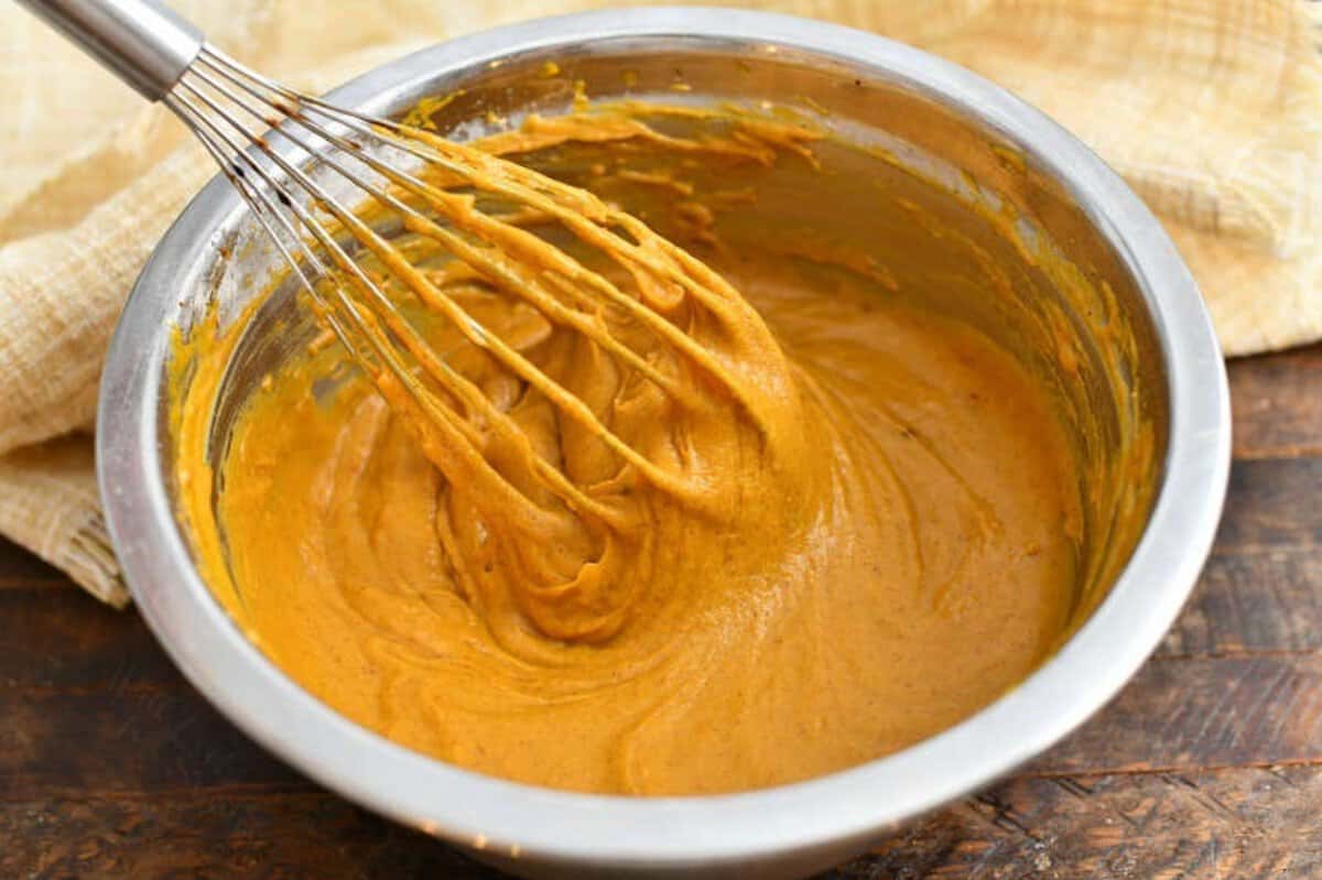 whisking pumpkin batter in a bowl to make a baked donuts recipe.