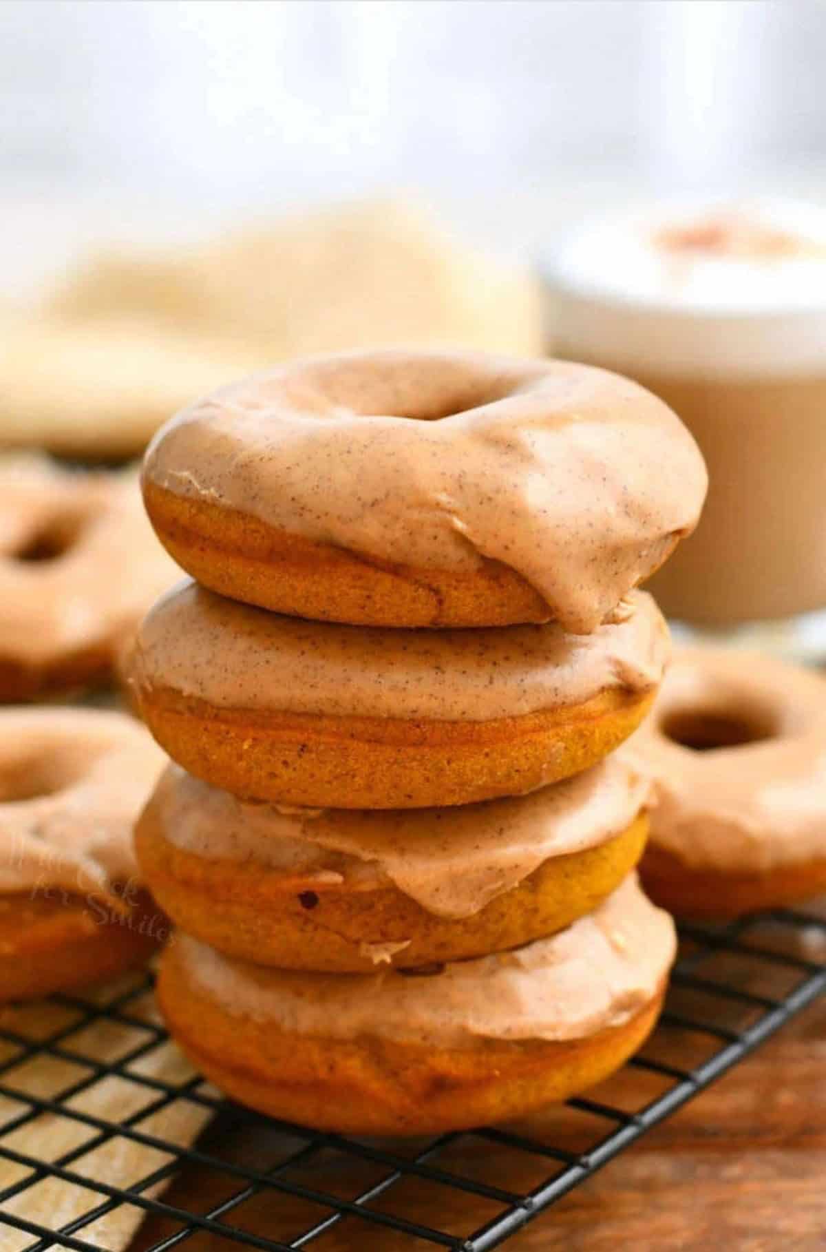 stack of four baked pumpkin donuts with pumpkin spice latte glaze on wire rack.