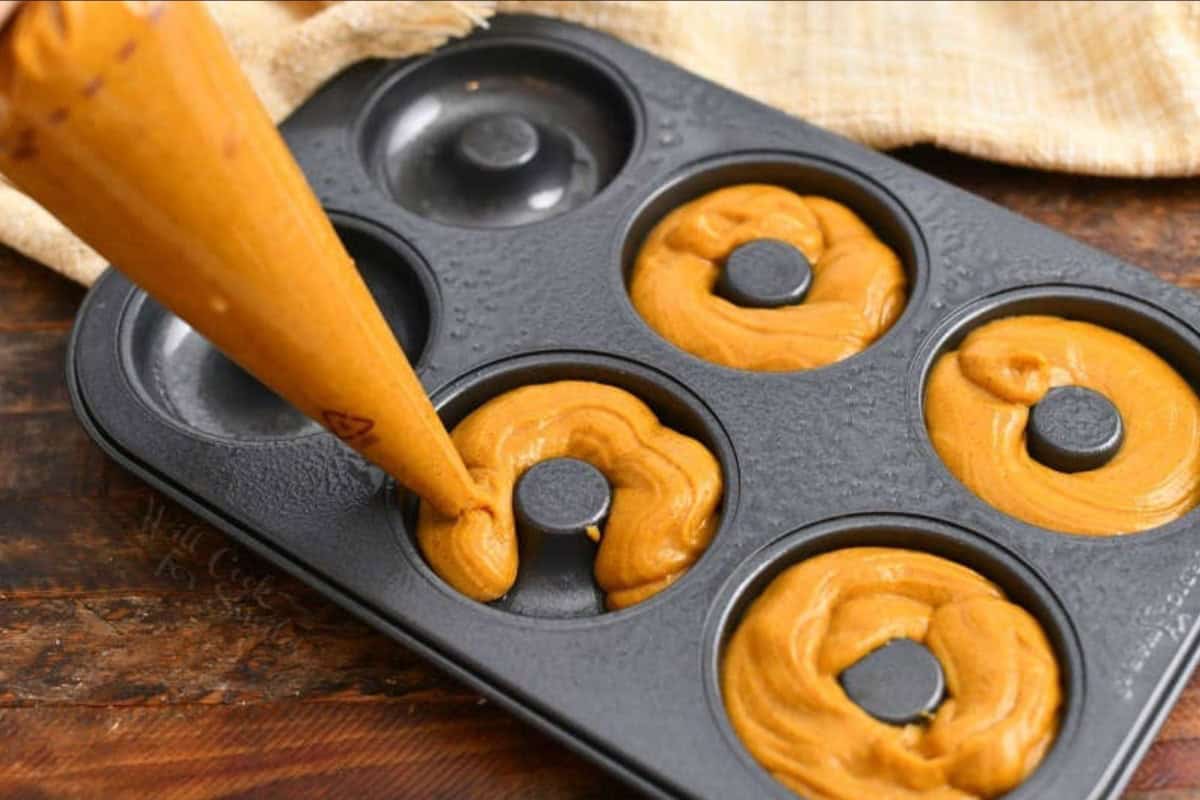 using pastry bag to fill the wells of donut pan for pumpkin spice latte baked donuts.