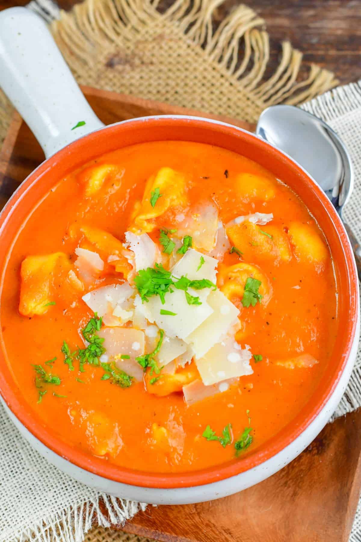 roasted red pepper soup in a bowl topped with shaved parmesan and parsley.