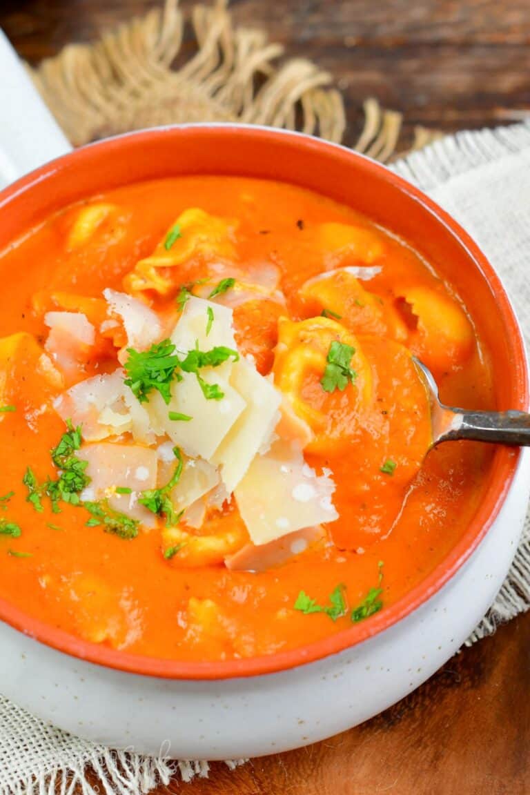 scooping out some red pepper soup and tortellini from a bowl.