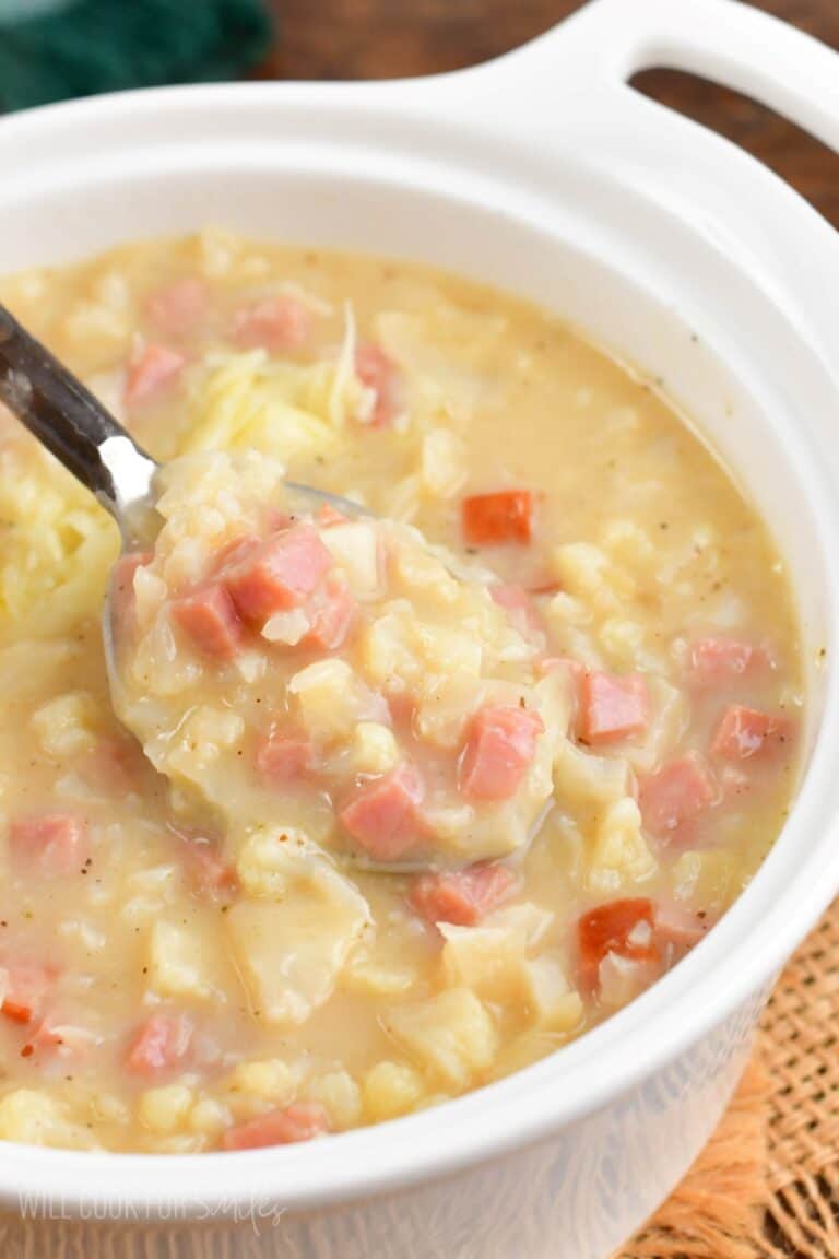 spooning cauliflower ham soup from a white bowl.